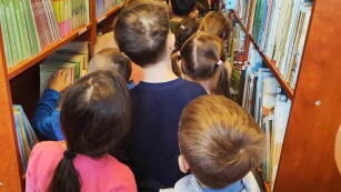 dzieci stoją pośrodku regałów biblioteki szkolnej