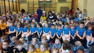 dzieci siedzą na sali gimnastycznej przed wystepem