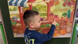 Dziecko  przykleja sylwetę papryki do plakatu „Witaminki”