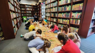 dzieci rysują własne książki, a w tle półki biblioteczne
